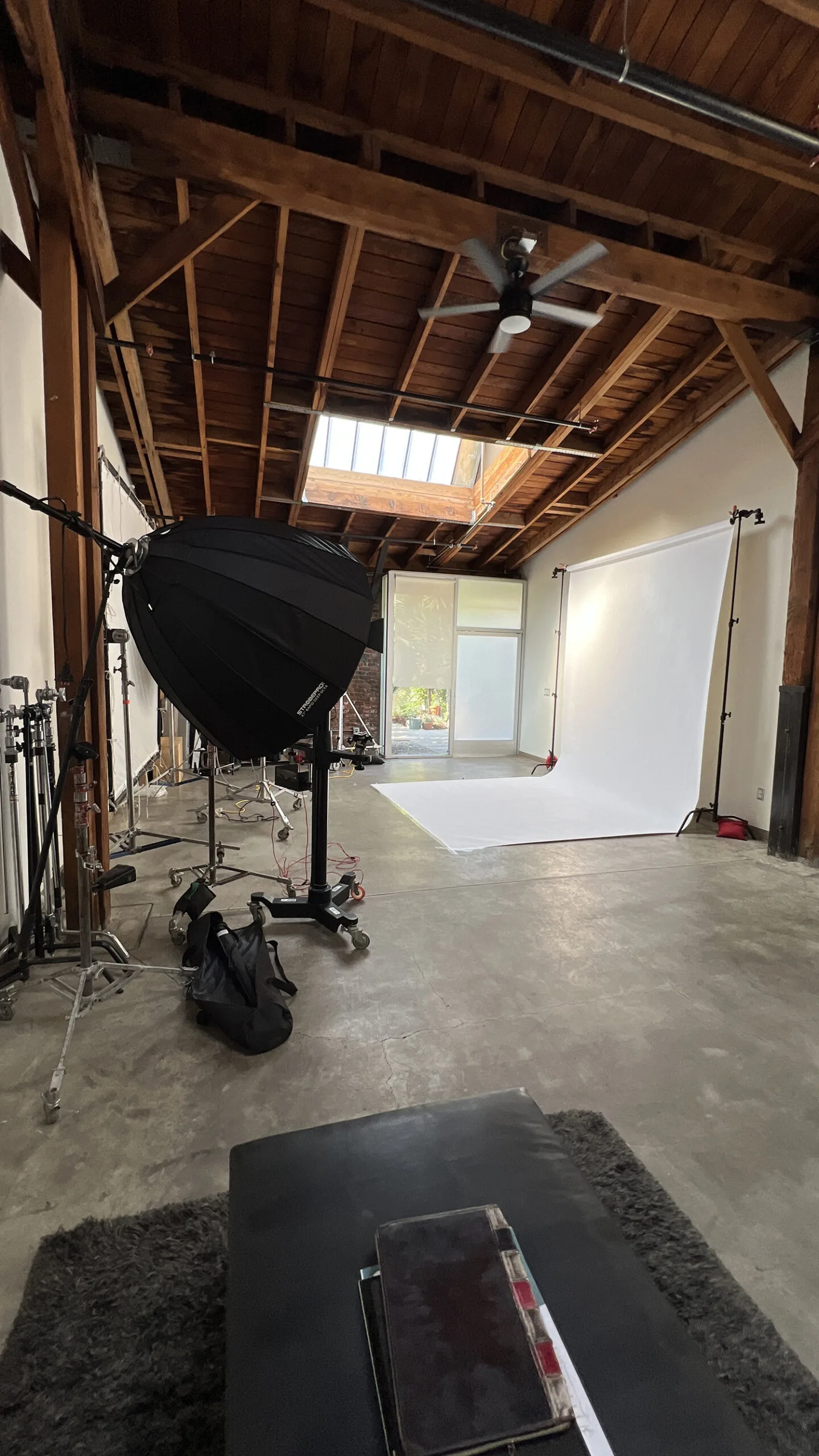 Interior view of Vidd Studios' spacious photography studio featuring a high wood beam ceiling with skylights, polished concrete floors, professional lighting equipment set up, and a large white cyclorama, ready for creative photo shoots.