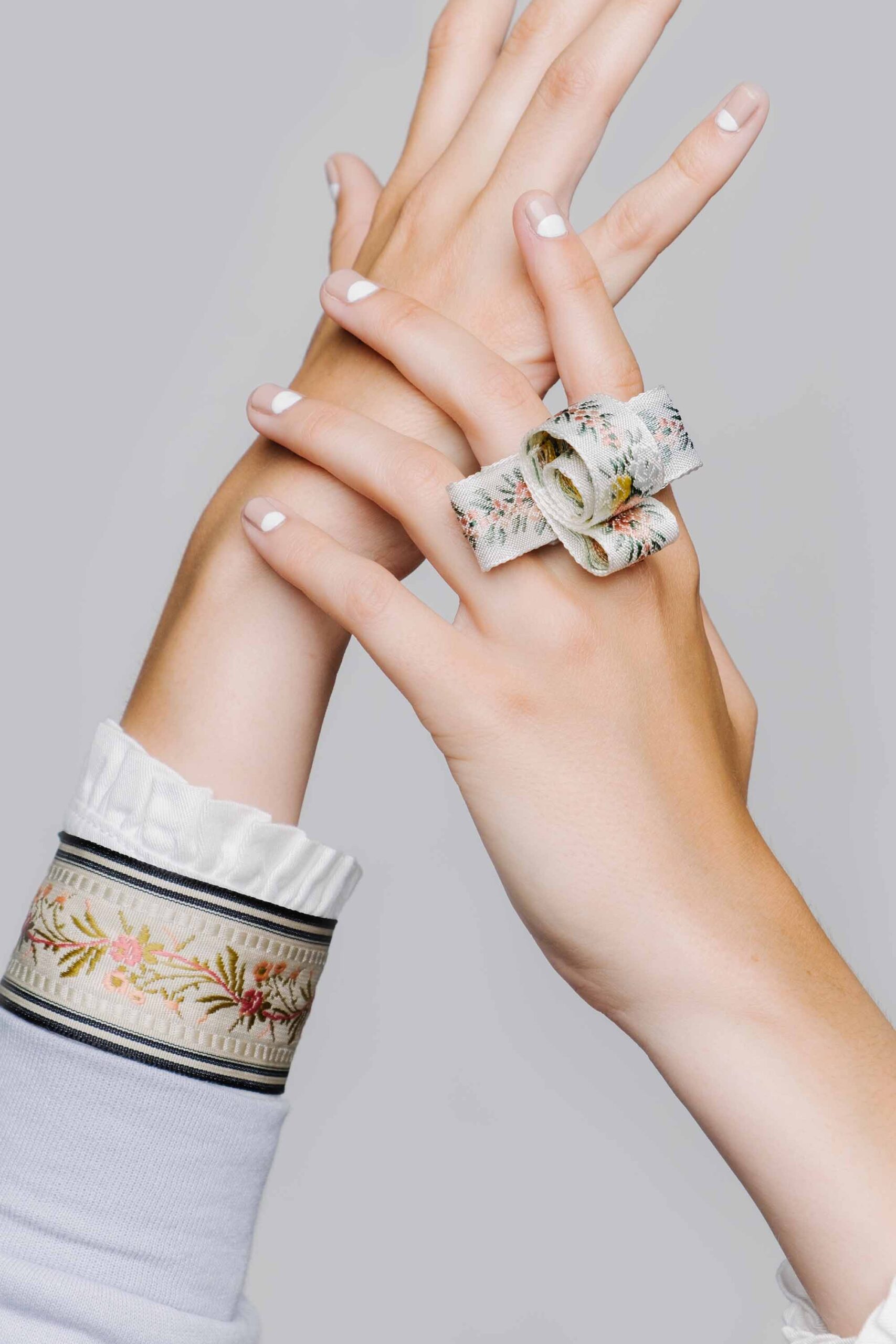 Art director in Los Angeles showcases minimalist elegance with a close-up of hands adorned with a floral fabric wrist accessory against a grey background.